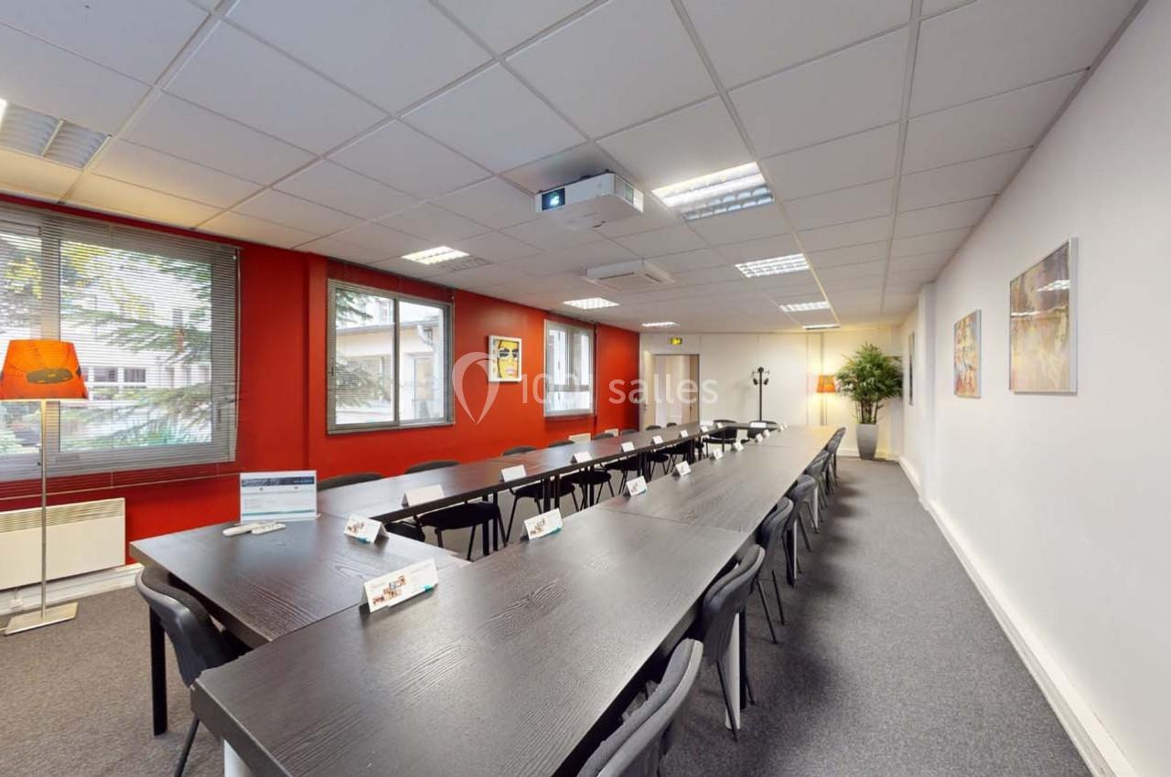 Salle de réunion lumineuse avec une grande table rectangulaire, chaises noires, projecteur au plafond et décoration sobre.