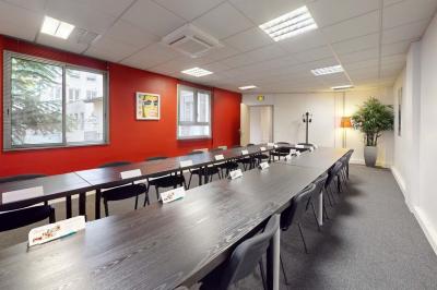 Salle de réunion avec une longue table rectangulaire, chaises noires, projecteur et murs blancs et rouges.