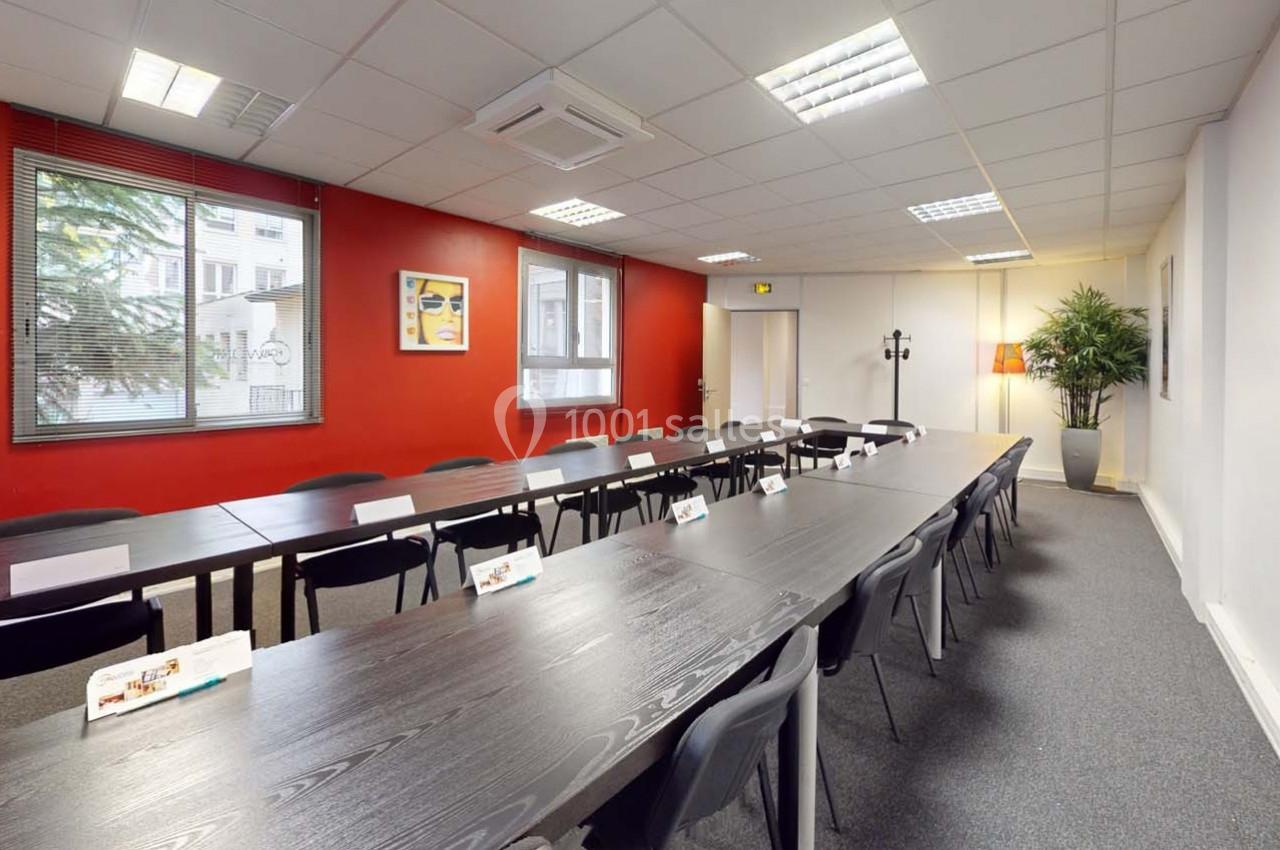 Salle de réunion lumineuse avec de longues tables noires, des chaises, des affiches murales et une plante décorative.