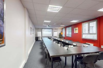 Salle de réunion avec une longue table rectangulaire, chaises noires, projecteur et murs blancs et rouges.