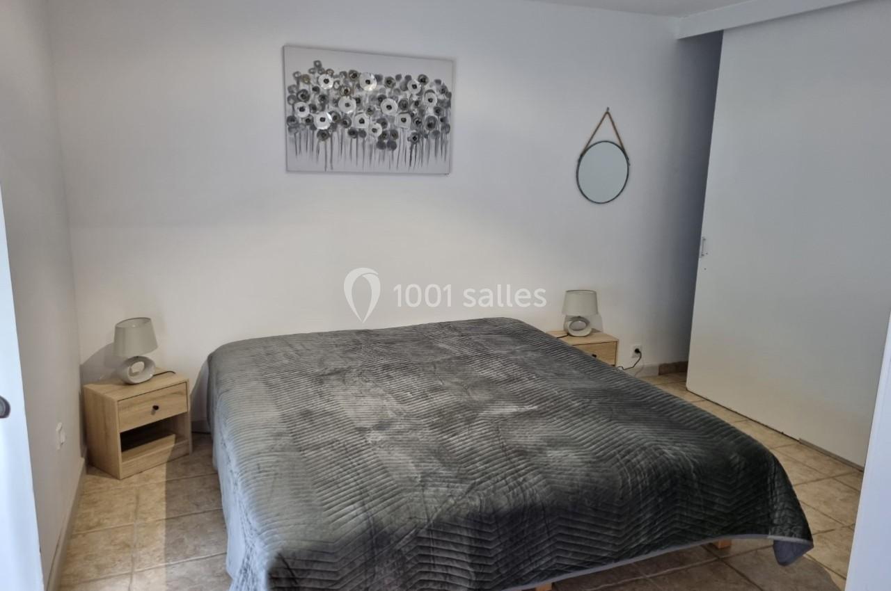 Chambre avec un lit double, couvre-lit gris, tables de chevet en bois, lampes et décoration murale sobre.