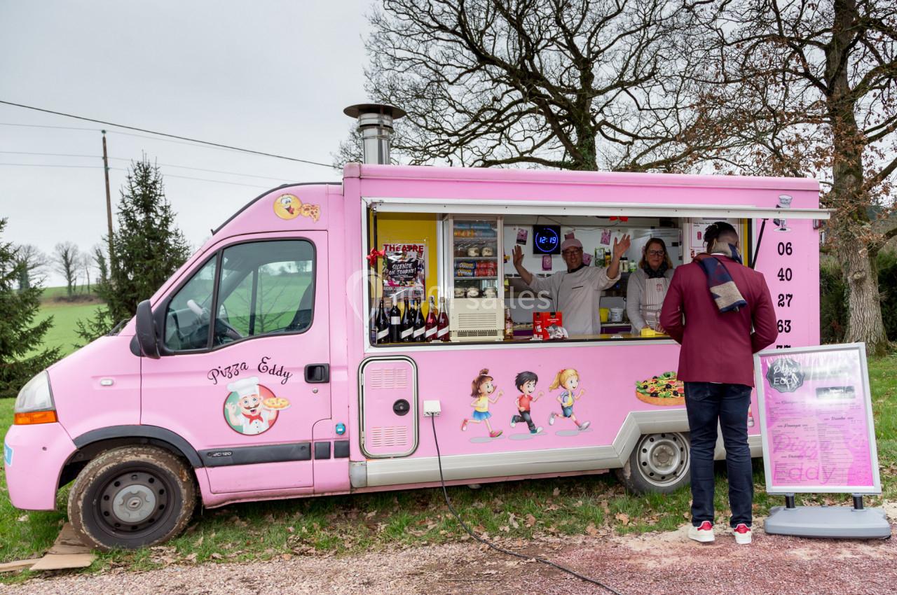Camion-restaurant rose servant des pizzas, avec un client commandant devant et deux personnes à l'intérieur.
