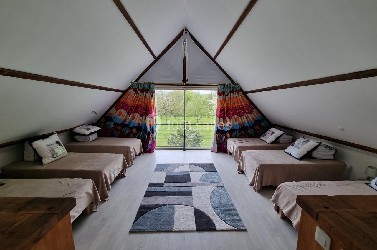 Intérieur d'une chambre mansardée avec six lits simples, tapis géométrique et vue sur un jardin par une baie vitrée.