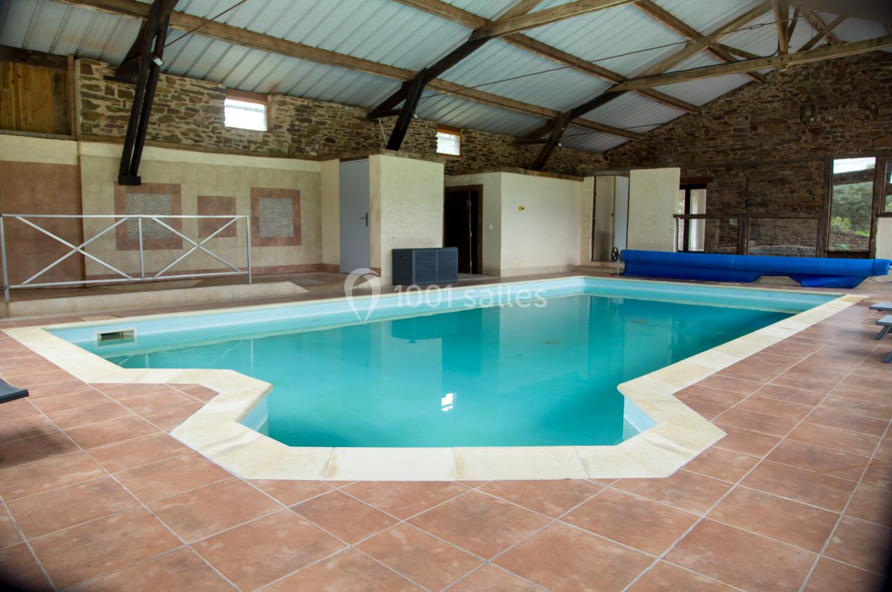 Piscine intérieure avec carrelage beige, entourée de murs en pierre et d'une charpente en bois apparente.