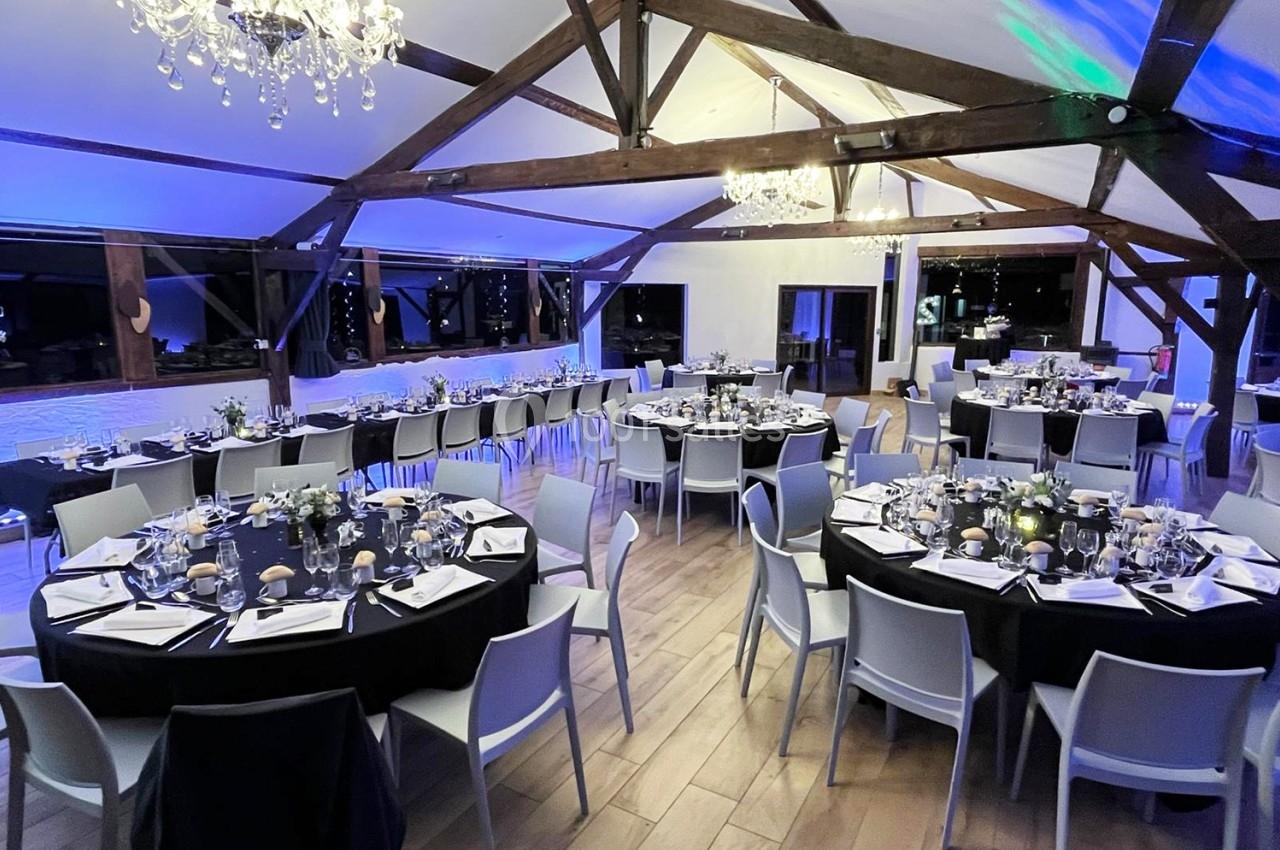 Salle de réception décorée avec des tables rondes dressées, chaises modernes et éclairage chaleureux sous une charpente en…