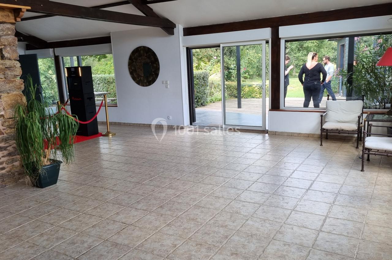 Salle lumineuse avec sol en carrelage, murs en pierre et grandes baies vitrées donnant sur un jardin.