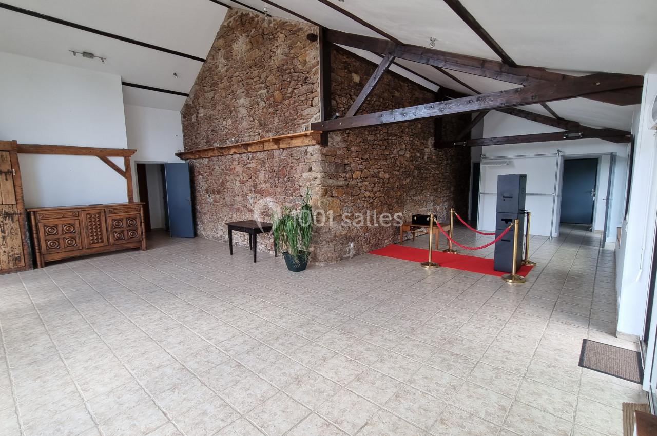 Salle lumineuse avec murs en pierre, poutres apparentes, carrelage beige, tapis rouge et mobilier en bois rustique.