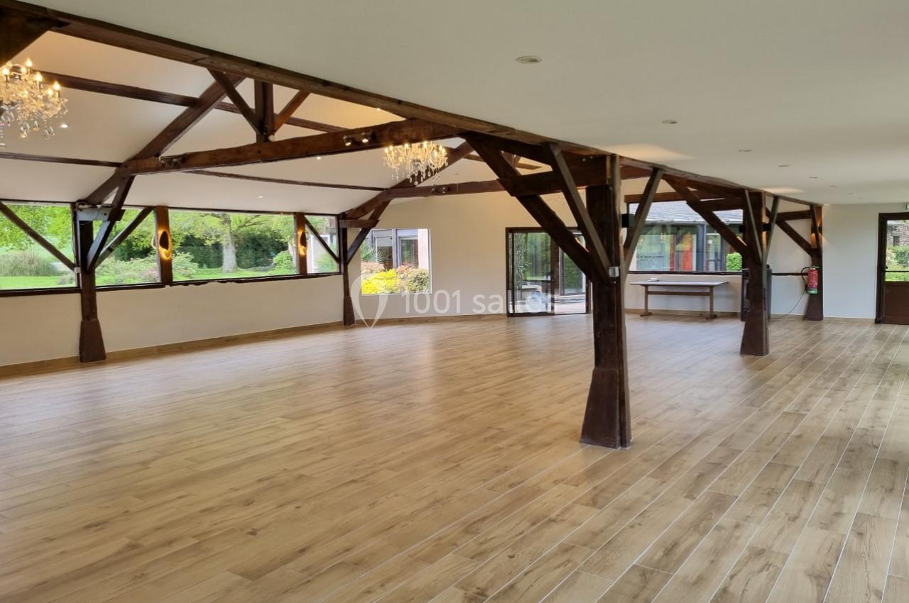 Salle spacieuse avec parquet en bois, poutres apparentes et grandes fenêtres donnant sur un jardin verdoyant.