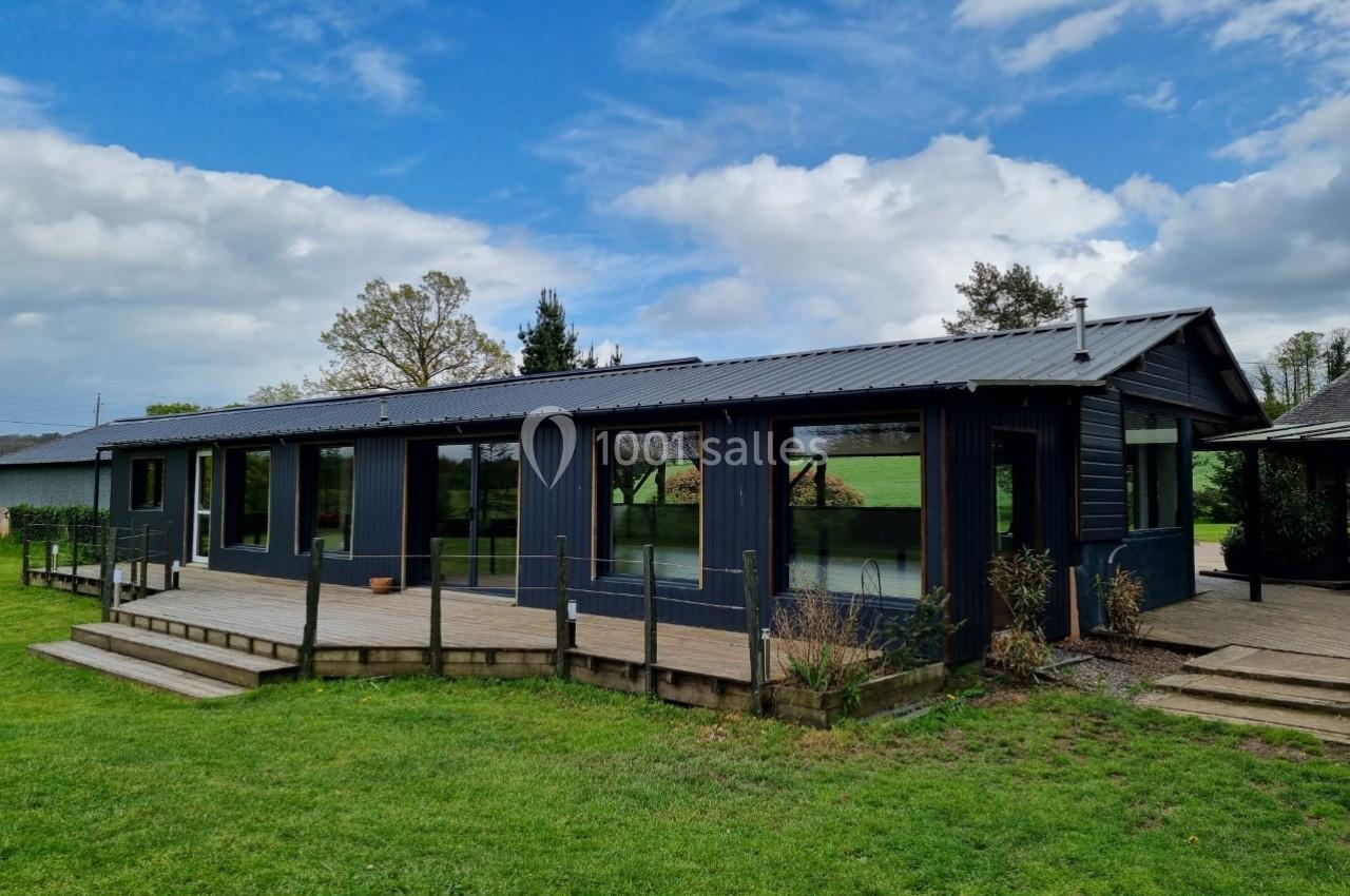 Maison moderne de plain-pied avec bardage sombre, grandes baies vitrées et terrasse en bois, entourée de verdure.