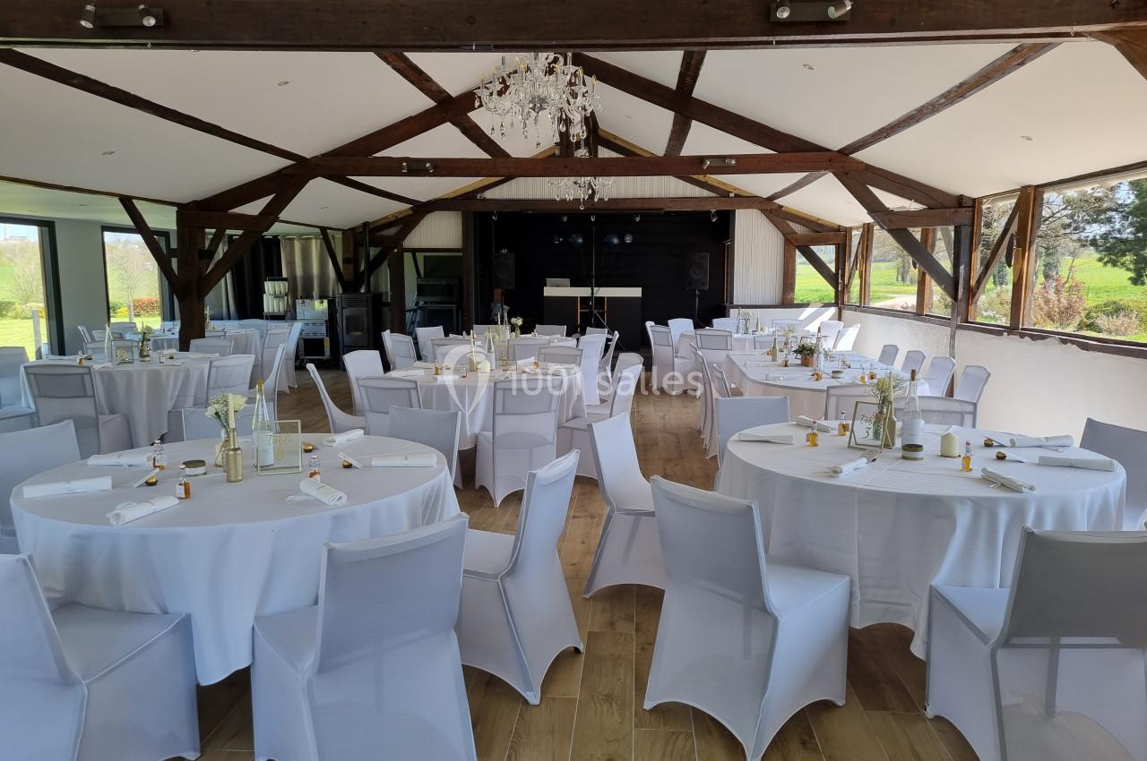 Salle de réception lumineuse avec tables rondes dressées de nappes blanches, chaises assorties et vue sur l'extérieur…