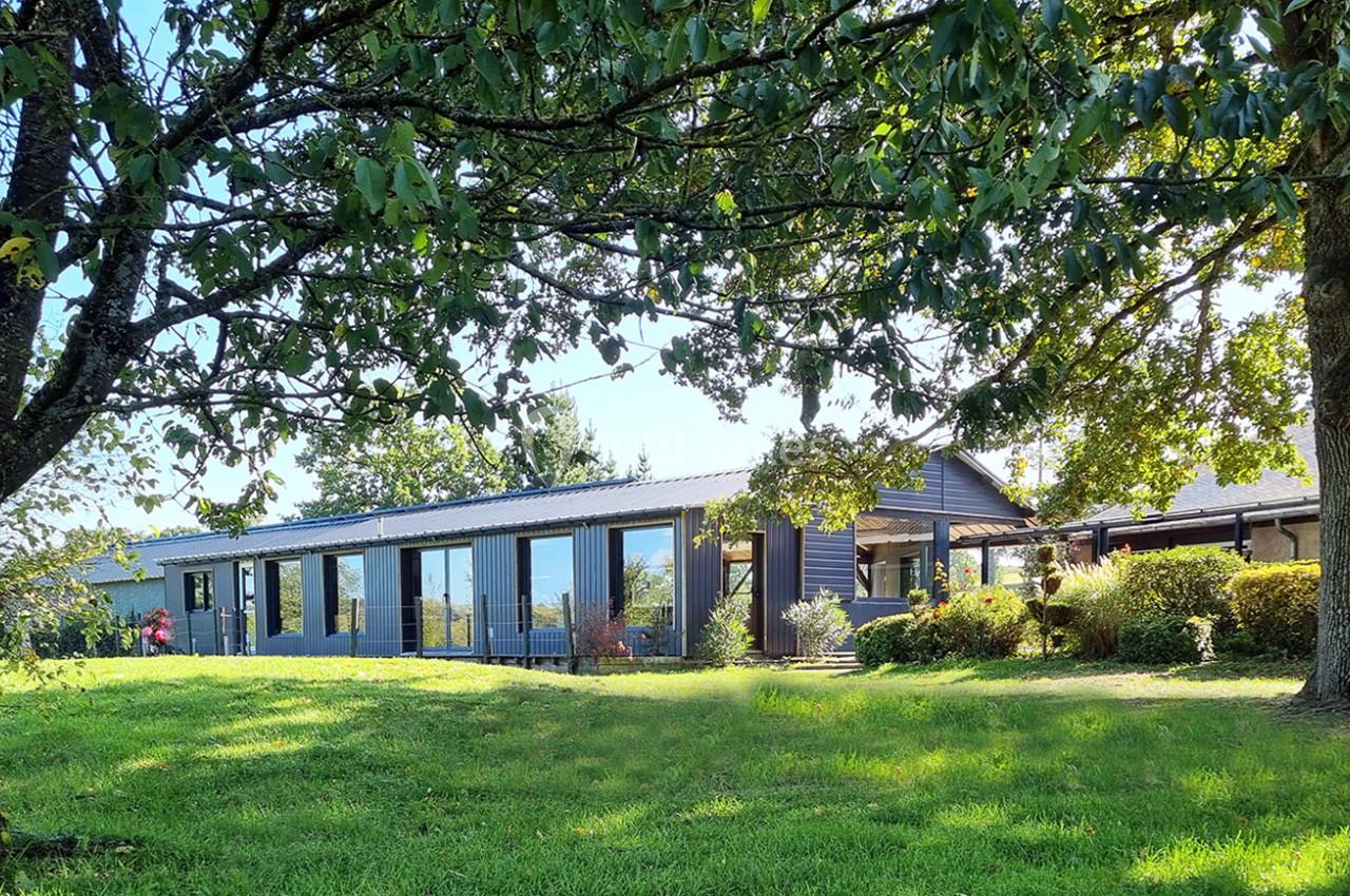 Bâtiment moderne avec de grandes baies vitrées entouré d'arbres et d'une pelouse verdoyante.