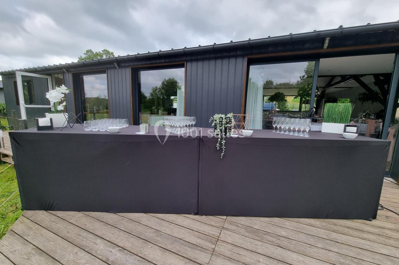 Table de service extérieure avec nappes noires, verres alignés et décorations florales, devant un bâtiment moderne.