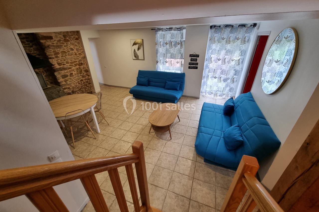 Vue d'un salon lumineux avec deux canapés bleus, une table basse, une table à manger et des rideaux imprimés.