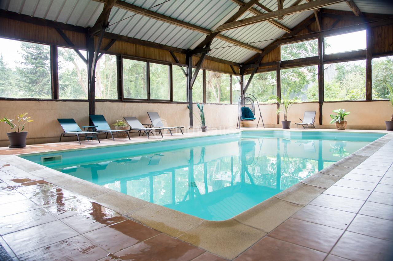 Piscine intérieure avec chaises longues, entourée de grandes baies vitrées donnant sur un espace arboré.