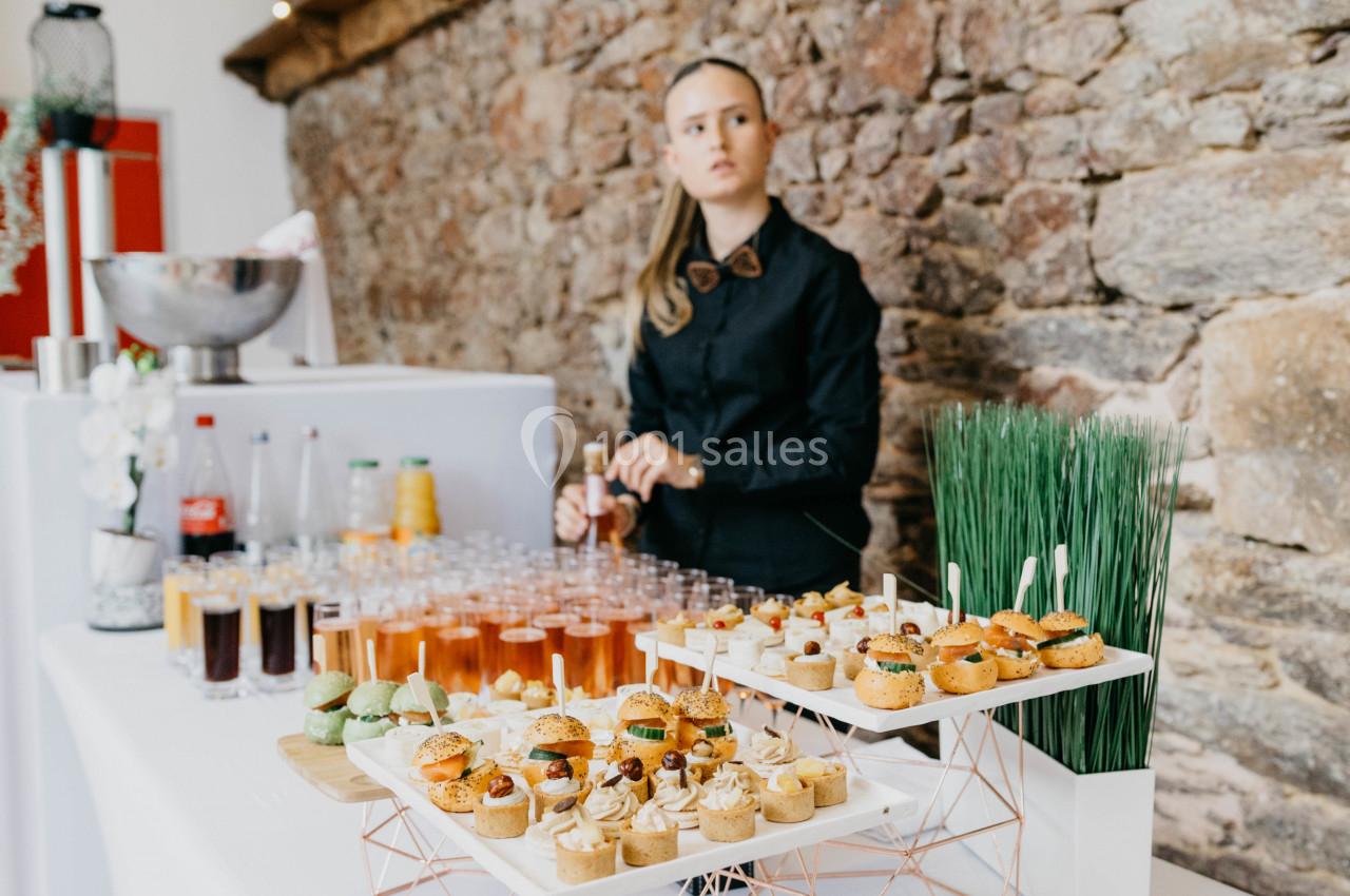Serveuse derrière une table de buffet garnie de cocktails, amuse-bouches et décorations dans un cadre en pierre.