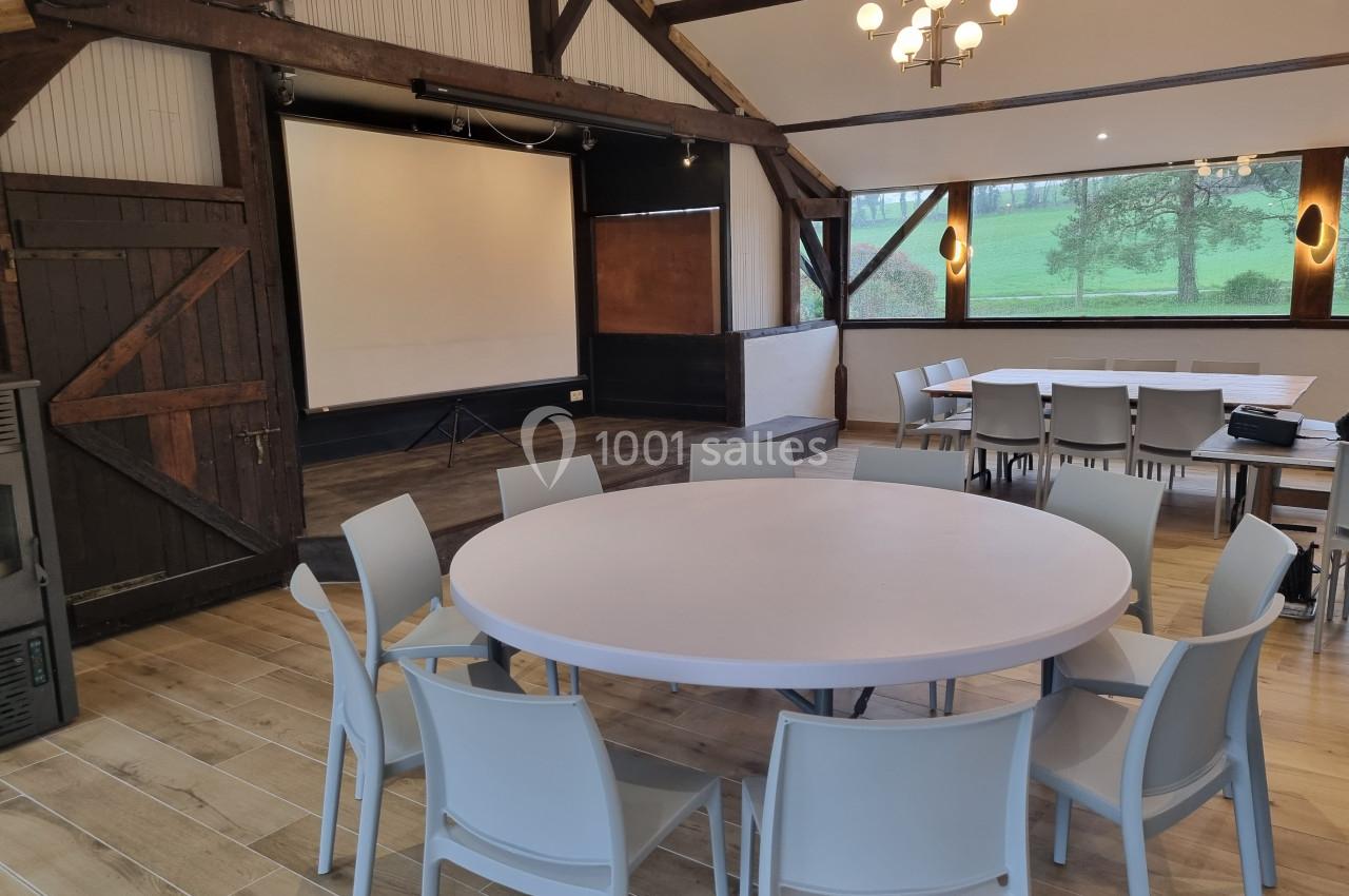 Salle de réunion avec tables rondes, chaises, écran de projection et vue sur un paysage extérieur verdoyant.