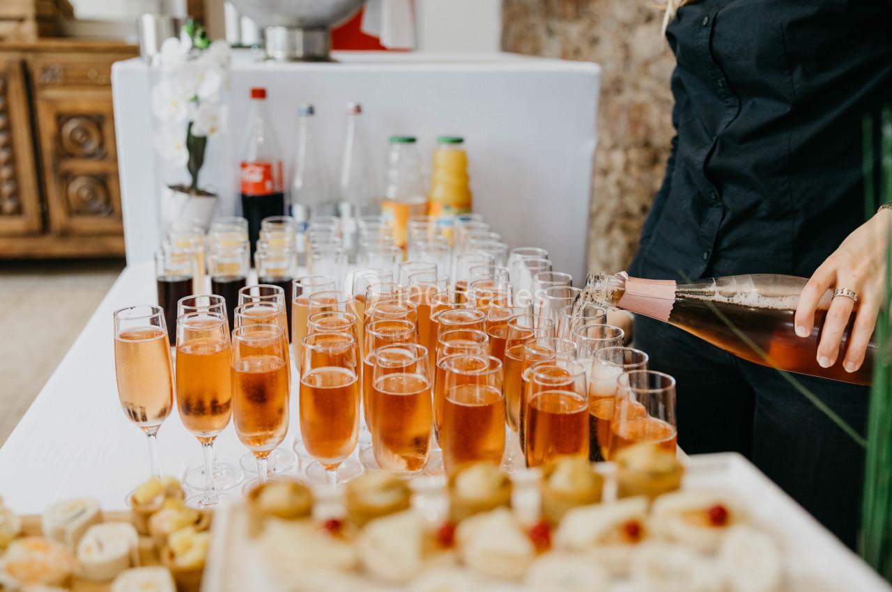 Une personne sert du vin pétillant rosé dans des flûtes alignées sur une table avec des boissons et amuse-bouches.