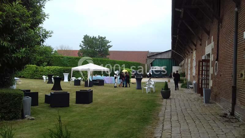 Cour extérieure avec pelouse, mobilier de jardin, barnum blanc et quelques personnes discutant près d'un bâtiment en briques.