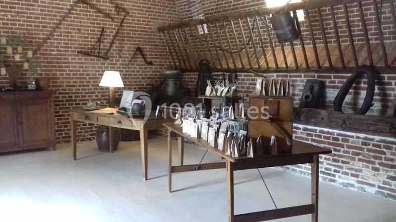 Salle rustique avec murs en briques, meubles en bois, objets anciens et étagères exposant des produits artisanaux.