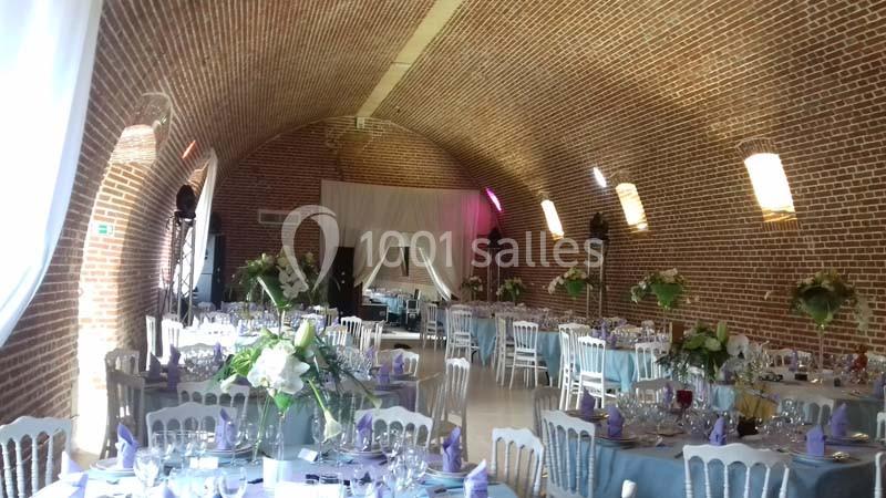 Salle voûtée en briques aménagée pour un événement, avec tables dressées et décorations florales.