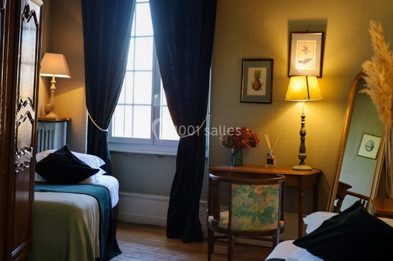Chambre avec deux lits, meubles en bois, lampes allumées, grande fenêtre avec rideaux sombres et décorations murales.