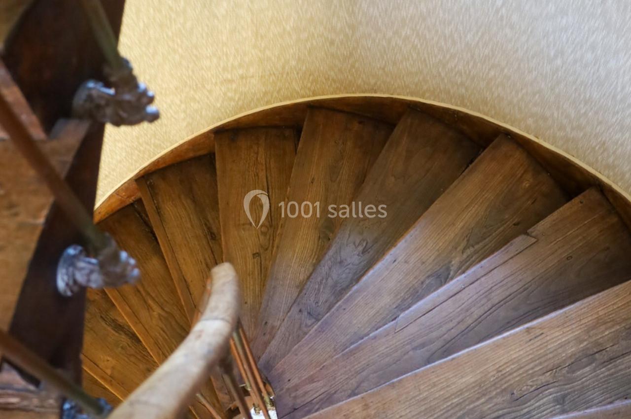 Escalier en bois en colimaçon vu de haut, avec une rampe en bois et un mur clair en arrière-plan.