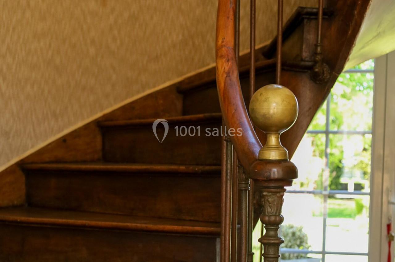 Escalier en bois ancien avec une rampe ornée d'une boule en laiton, éclairé par une porte vitrée donnant sur un jardin.