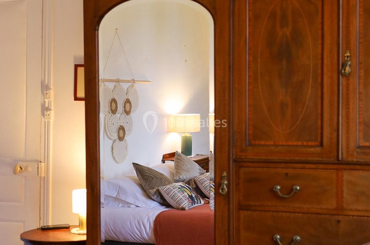 Reflet d'une chambre avec lit, coussins colorés, attrape-rêves au mur et mobilier en bois.