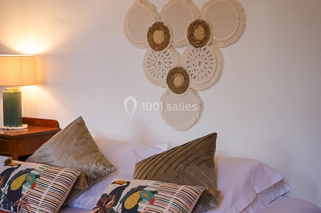 Lit avec coussins colorés et décoration murale en macramé dans une chambre lumineuse.