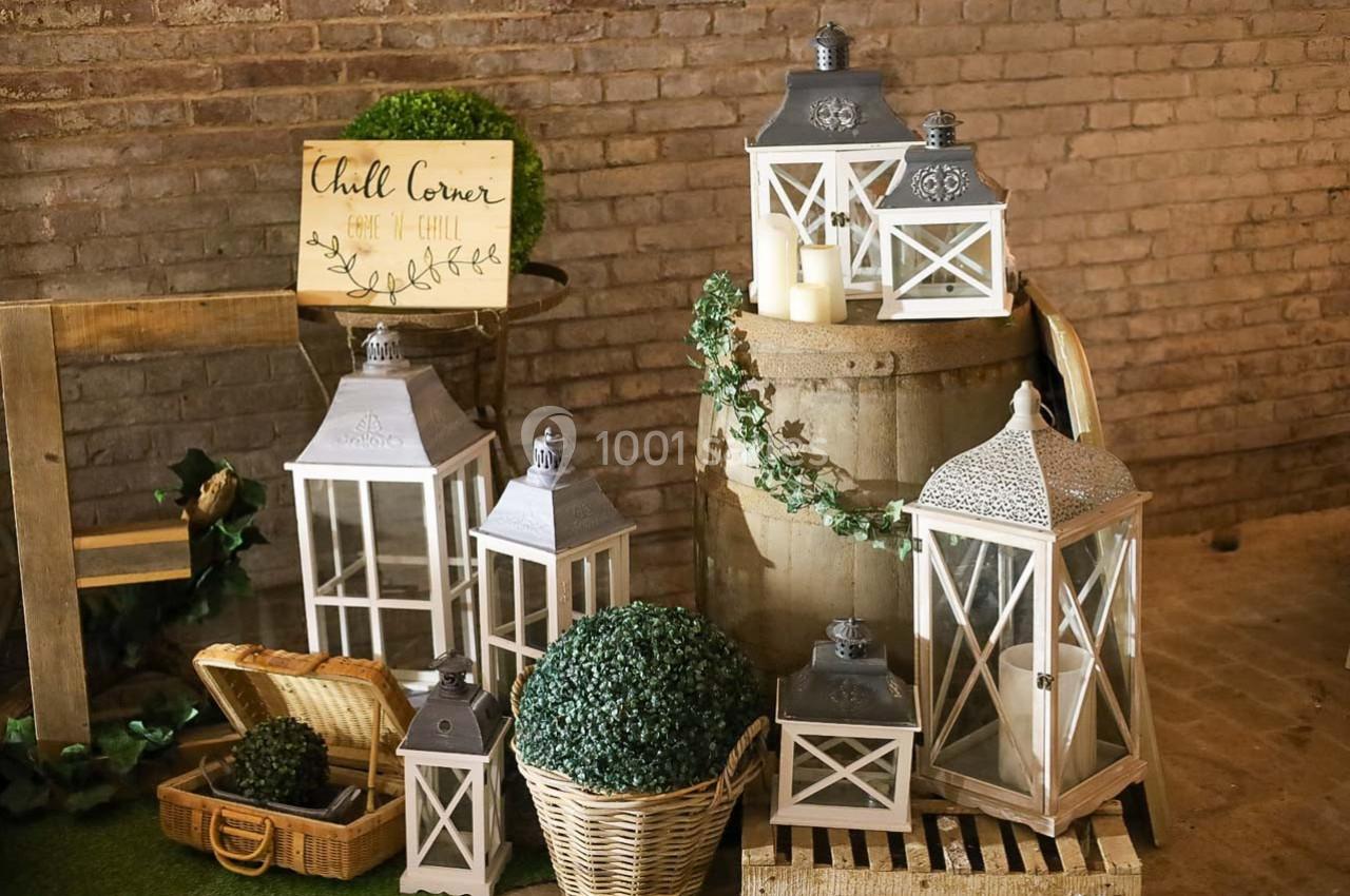 Lanternes blanches décoratives posées sur un tonneau et des paniers, entourées de plantes et bougies dans un décor rustique.