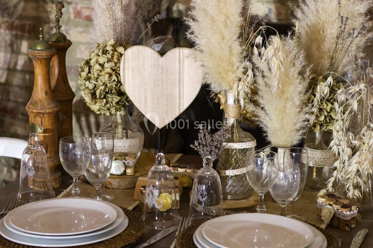 Table décorée avec des éléments rustiques, comprenant des assiettes, des verres, des fleurs séchées et un cœur en bois.