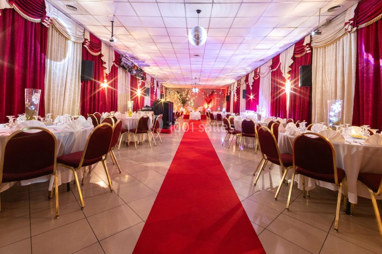 Salle de réception décorée avec des tables dressées, un tapis rouge central et des rideaux rouges et dorés.