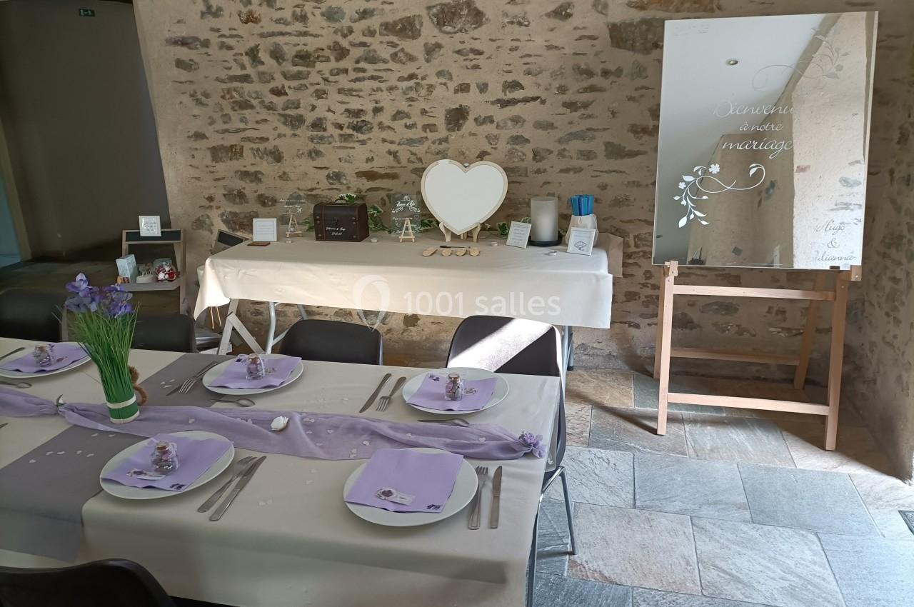 Table décorée pour un mariage avec nappes violettes, fleurs, et un miroir inscrit dans une salle en pierre.