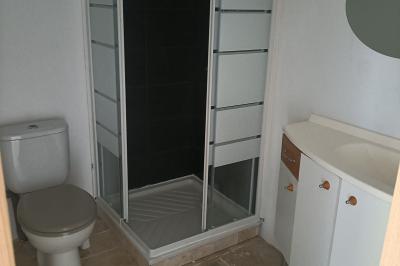 Lit double avec une couette blanche dans une chambre mansardée aux murs en pierre et plafond en bois.