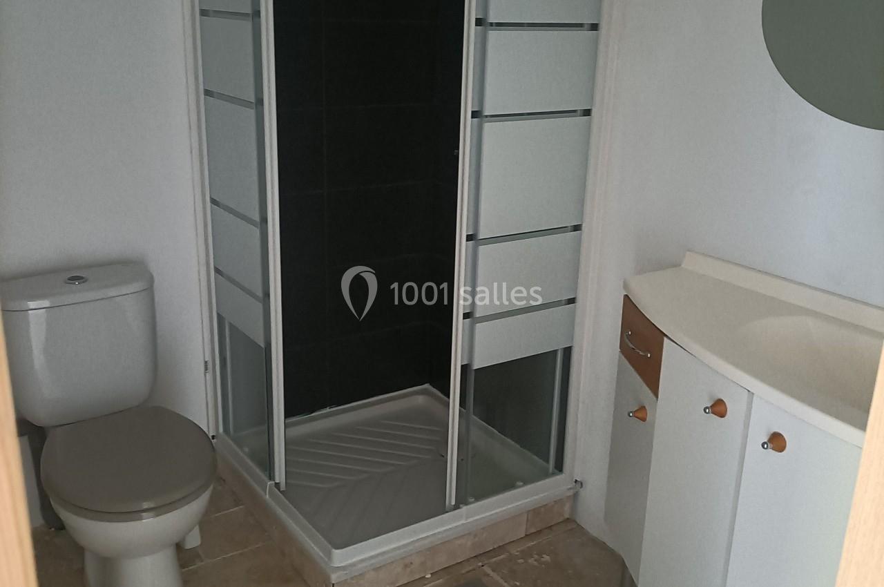 Salle de bain avec douche vitrée, lavabo avec meuble blanc et toilettes sur un sol en carrelage beige.