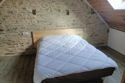 Lit double avec une couette blanche dans une chambre mansardée aux murs en pierre et plafond en bois.