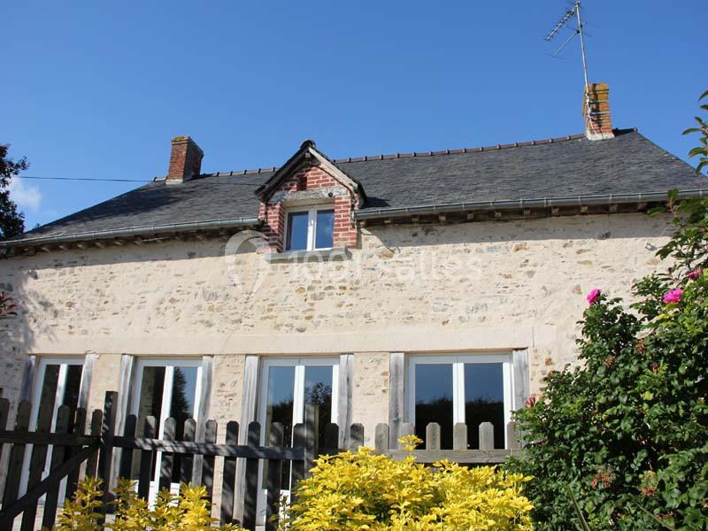 Façade d'une maison en pierre avec toit en ardoise, fenêtres blanches et jardin fleuri au premier plan.