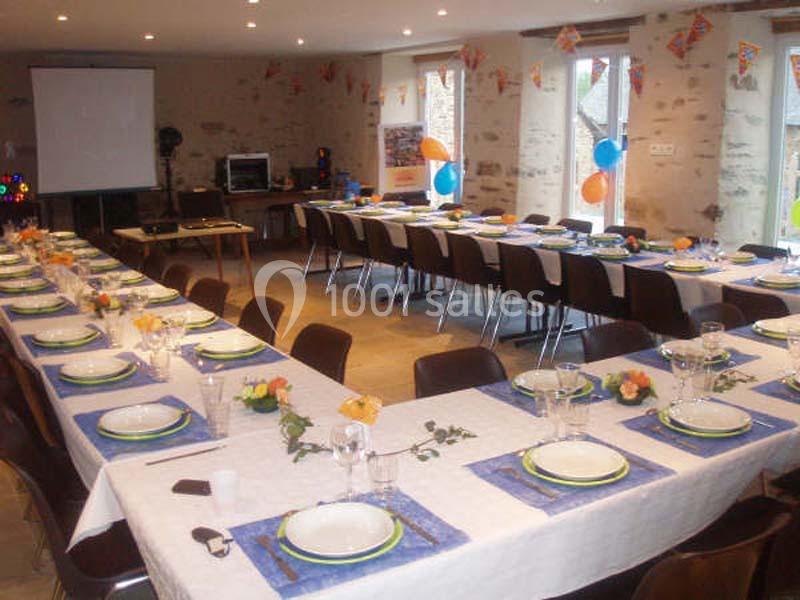 Salle décorée pour un événement, avec de longues tables dressées, nappes blanches, assiettes et décorations colorées.