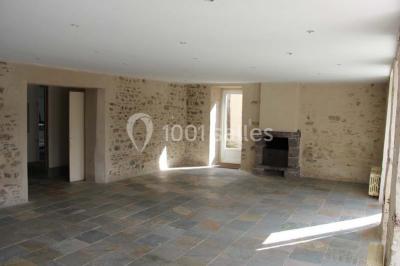 Lit double avec une couette blanche dans une chambre mansardée aux murs en pierre et plafond en bois.