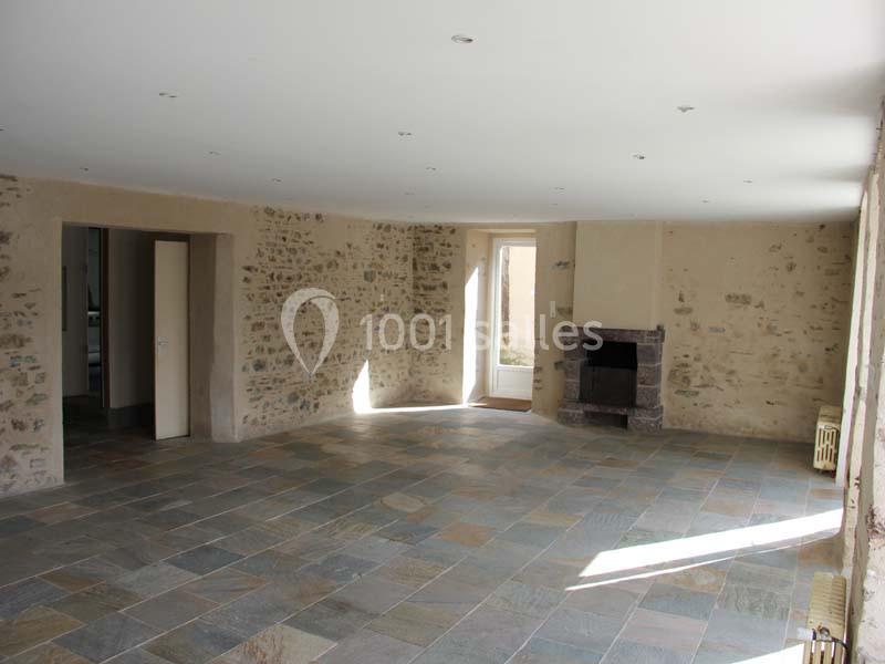 Salle lumineuse avec murs en pierre apparente, sol en dalles de pierre et une cheminée en pierre dans un coin.