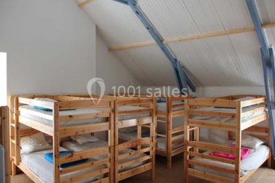 Lit double avec une couette blanche dans une chambre mansardée aux murs en pierre et plafond en bois.