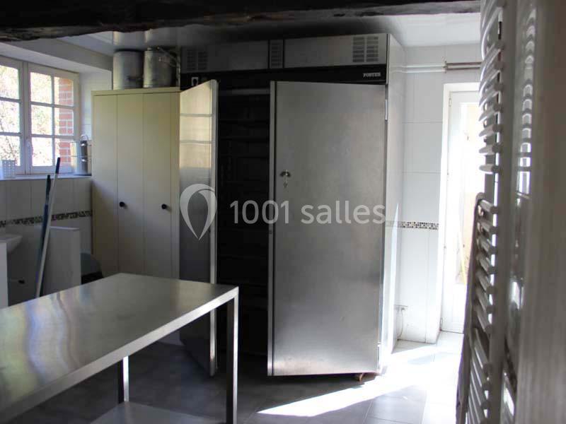 Cuisine professionnelle avec un grand réfrigérateur en acier inoxydable, une table en métal et des placards blancs.