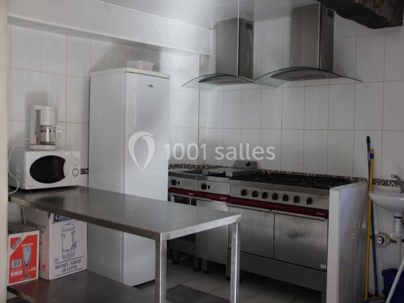 Cuisine équipée avec réfrigérateur, micro-ondes, cafetière, plan de travail en inox, cuisinière professionnelle et hotte.