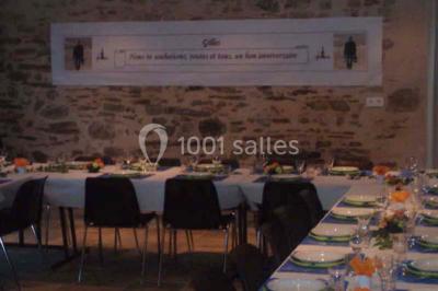 Lit double avec une couette blanche dans une chambre mansardée aux murs en pierre et plafond en bois.