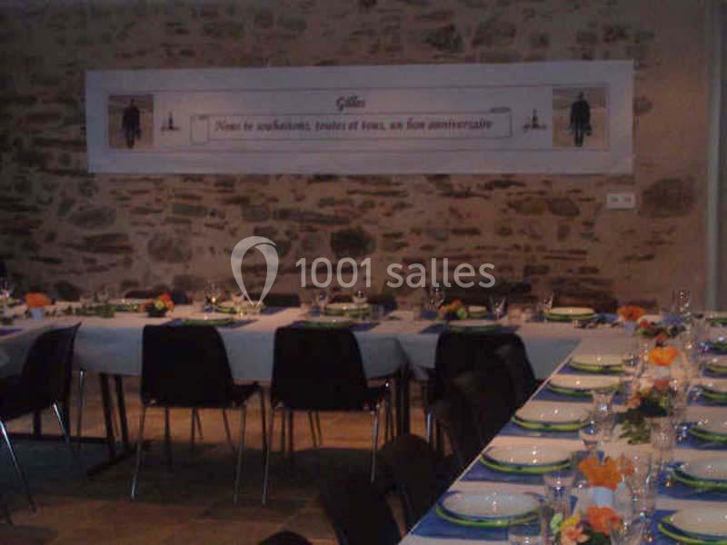 Salle décorée pour un anniversaire avec tables dressées, nappes blanches et bleues, et centres de table fleuris.