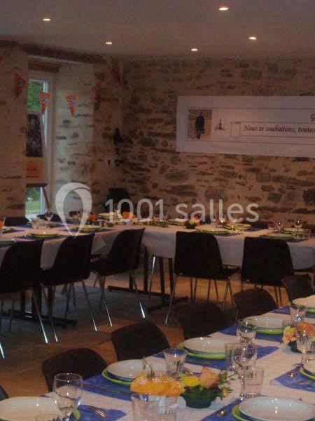 Salle décorée avec des tables dressées pour un repas, avec nappes bleues, vaisselle et murs en pierre apparente.