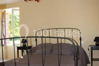 Lit double avec une couette blanche dans une chambre mansardée aux murs en pierre et plafond en bois.