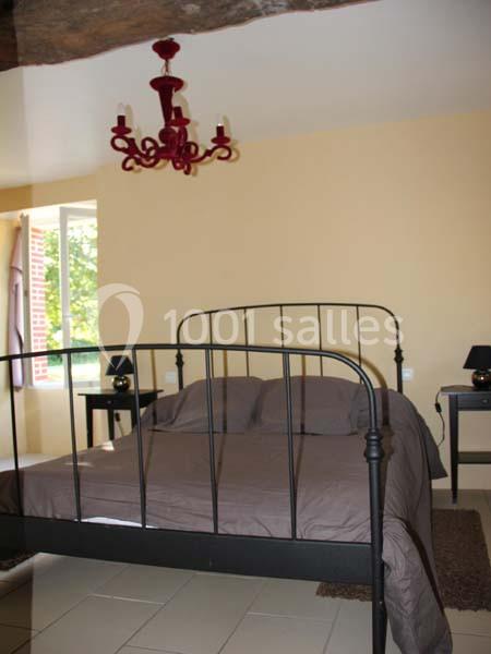 Lit en métal noir avec une couverture grise dans une chambre lumineuse, décorée d'un lustre rouge et de tables de chevet.