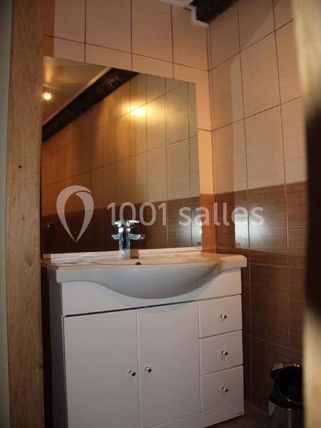 Lavabo blanc avec meuble de rangement intégré, miroir rectangulaire et carrelage beige dans une petite salle de bain.