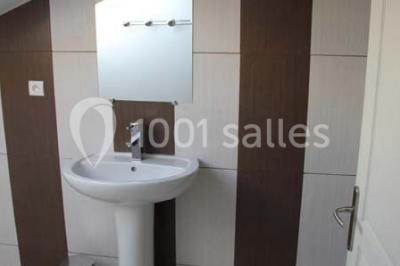 Lit double avec une couette blanche dans une chambre mansardée aux murs en pierre et plafond en bois.